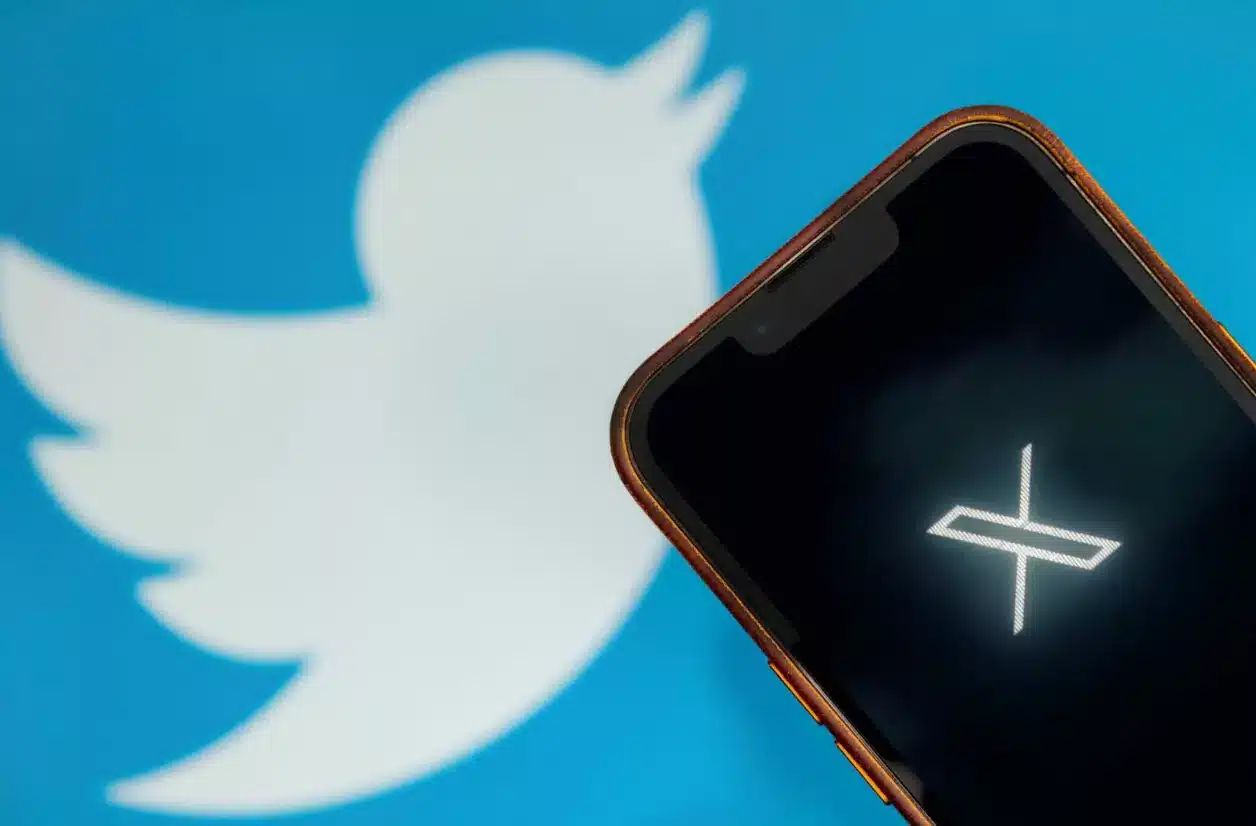 هاتفٌ محمولٌ يوضّح شعار منصة X وفي الخلفية يوجد شعار تويتر