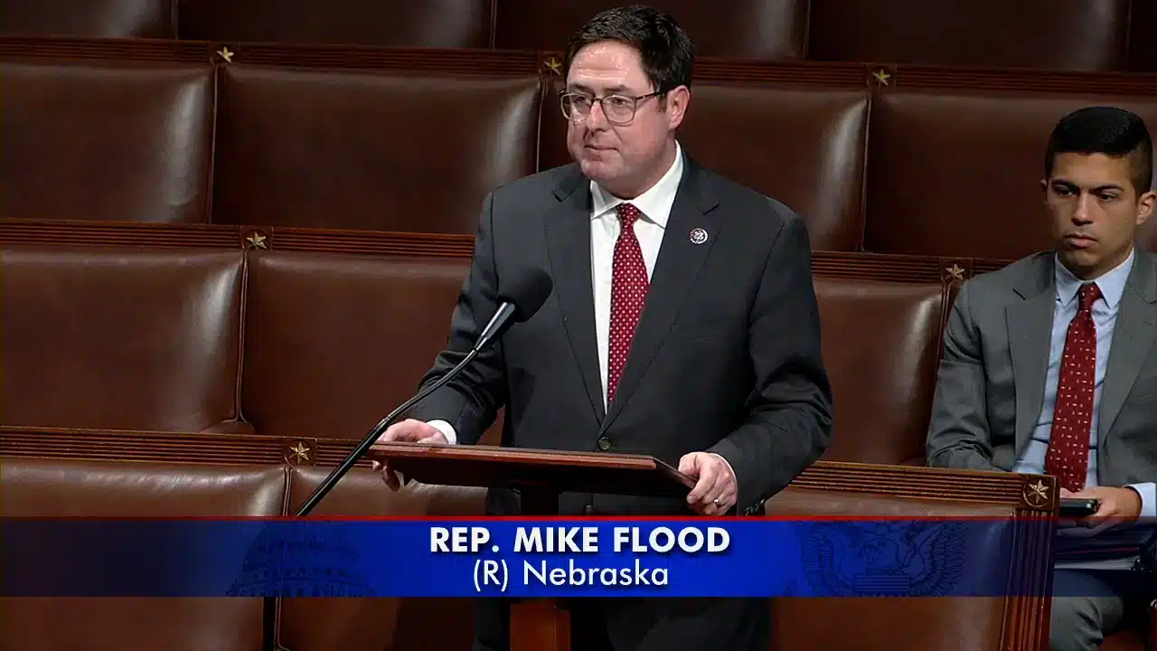 صورةٌ للنائب مايك فلود (Mike Flood) في قاعة مجلس الكونجرس متحدثاً وخلفه رجلٌ جالس في مقعده