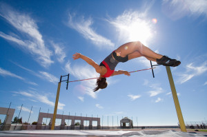 Female athlete jumping over bar, low angle view (lens flare)