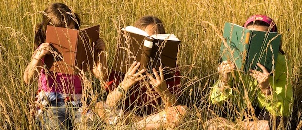 three 5 year old girls reading books in a meadow