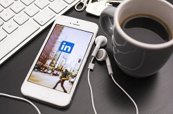 A smartphone, computer, and cup of coffee all sit on a desk; each of these items are necessary social media management tools.