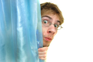 Man with glasses peeks behind a curtain with wide eyes. There is pure white copyspace to the right of him.