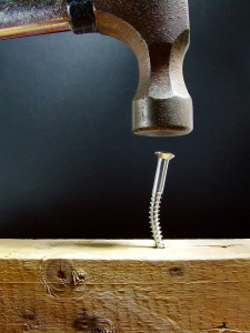 An apparent foolish attempt to hammer a screw into a piece of wood (an example of using the wrong tool for the job).