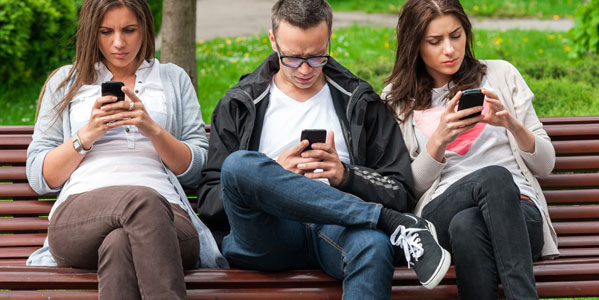 mobile-blog-two-women-and-a-man-sitting-on-a-bench-in-a-park-looking-at-their-phones