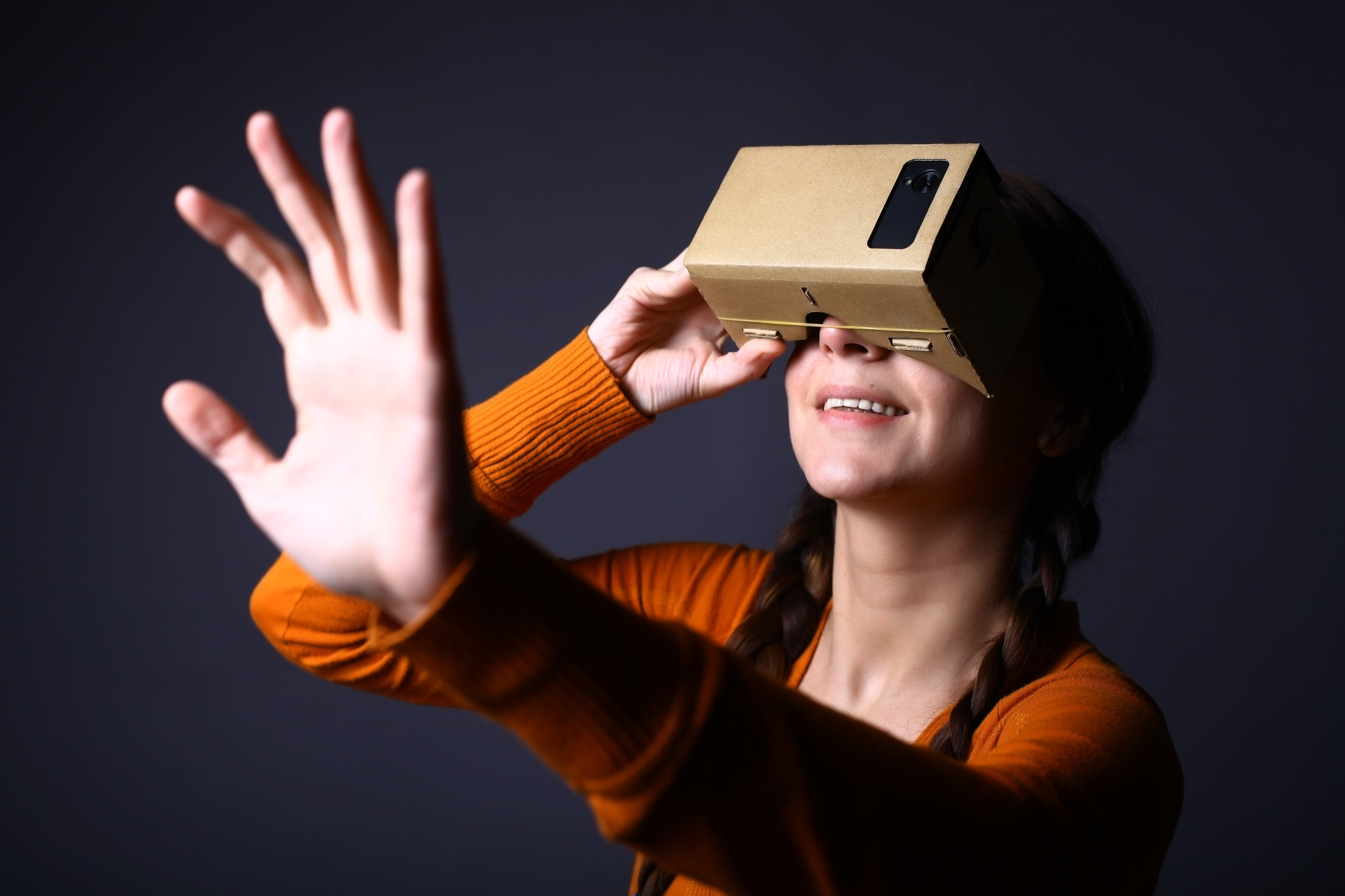 Color shot of a young woman looking through a cardboard, a device with which one can experience virtual reality on a mobile phone.