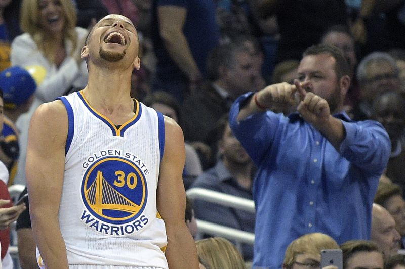 Stephen Curry of the Golden State Warriors celebrates while a fan reacts in the background.