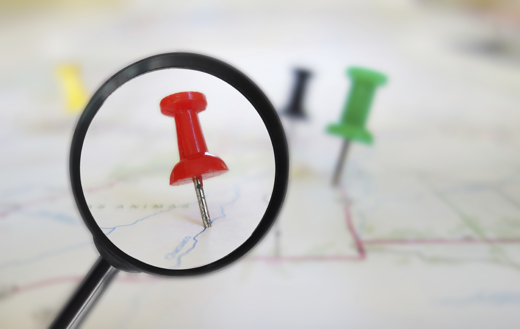 Magnifying glass closeup of push pin tacks in a map