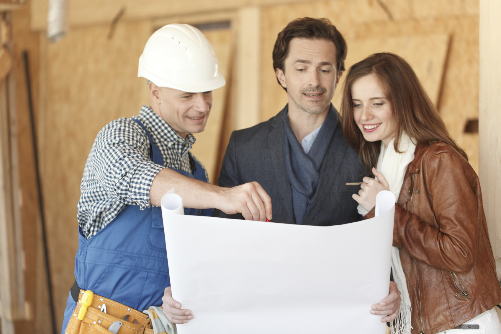 Worker shows house design plans to a young couple at construction site