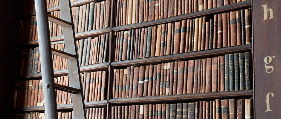 Photo of shelves of antique library books with a ladder for the top shelves