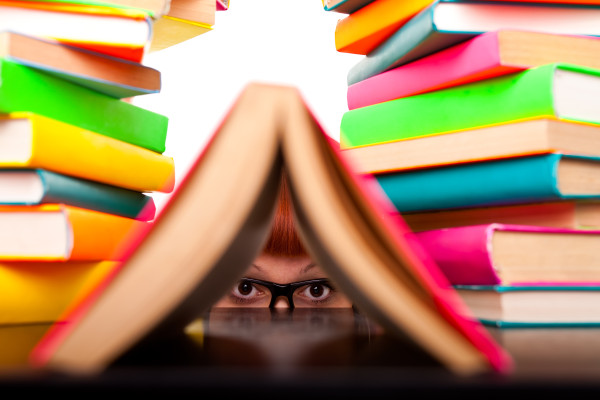 schoolgirl peeking behind books, funny concept, isolated on white