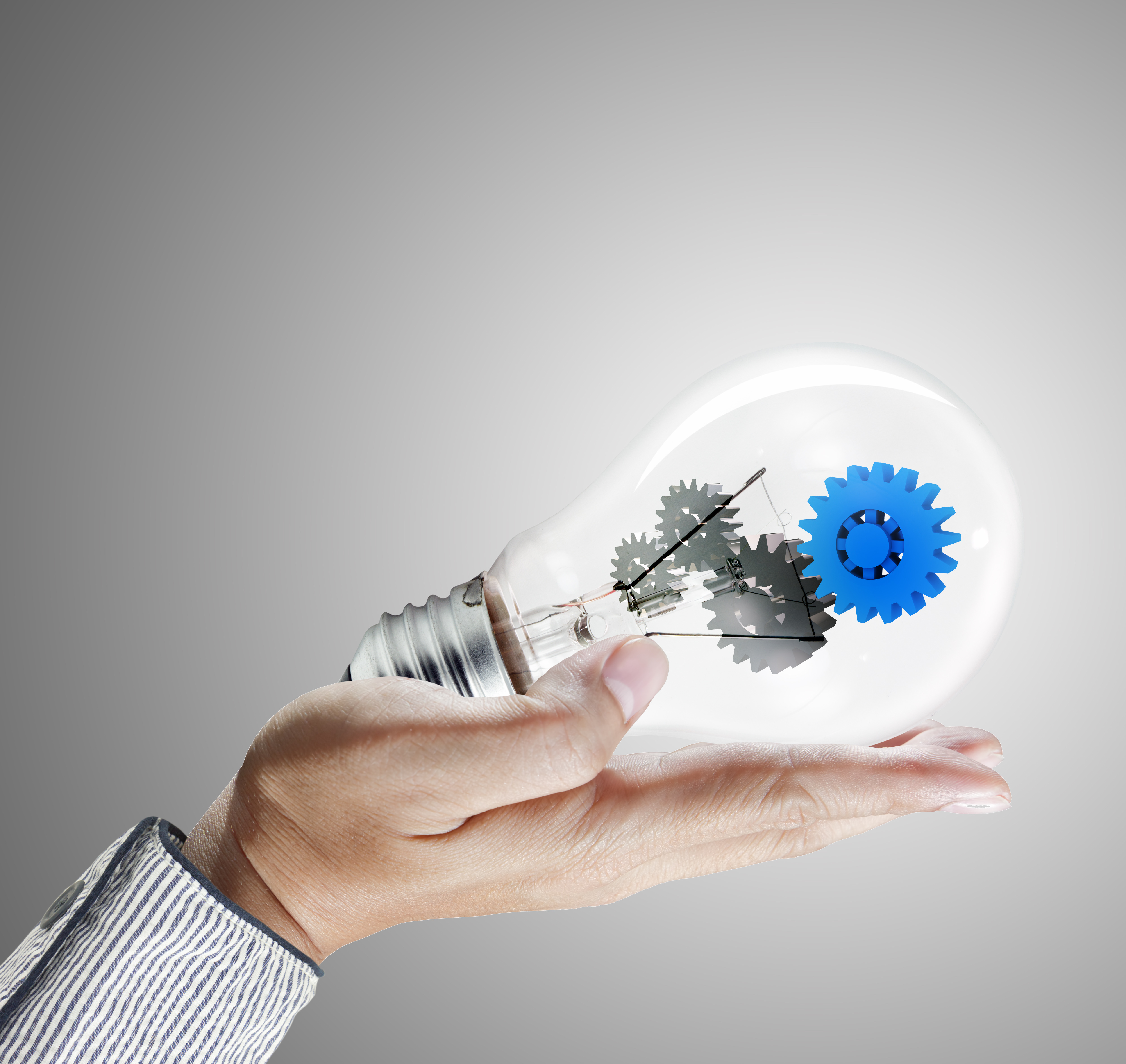 hand holds blue gear in light bulb