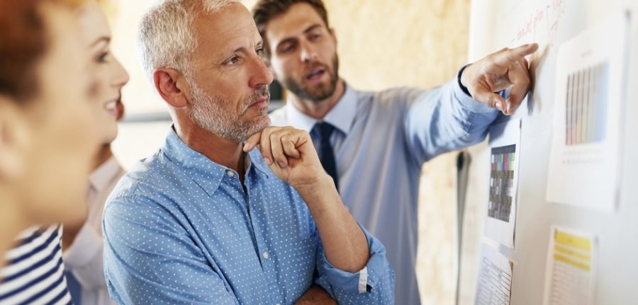 group of businesspeople looking at graphs pinned on a wall and considering their options