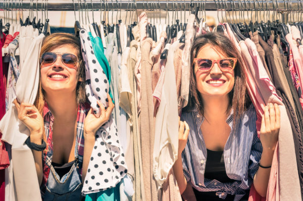 Young beautiful women at the weekly cloth market - best friends sharing free time having fun and shopping in the old town in a sunny day - girlfriends enjoying everyday life moments
