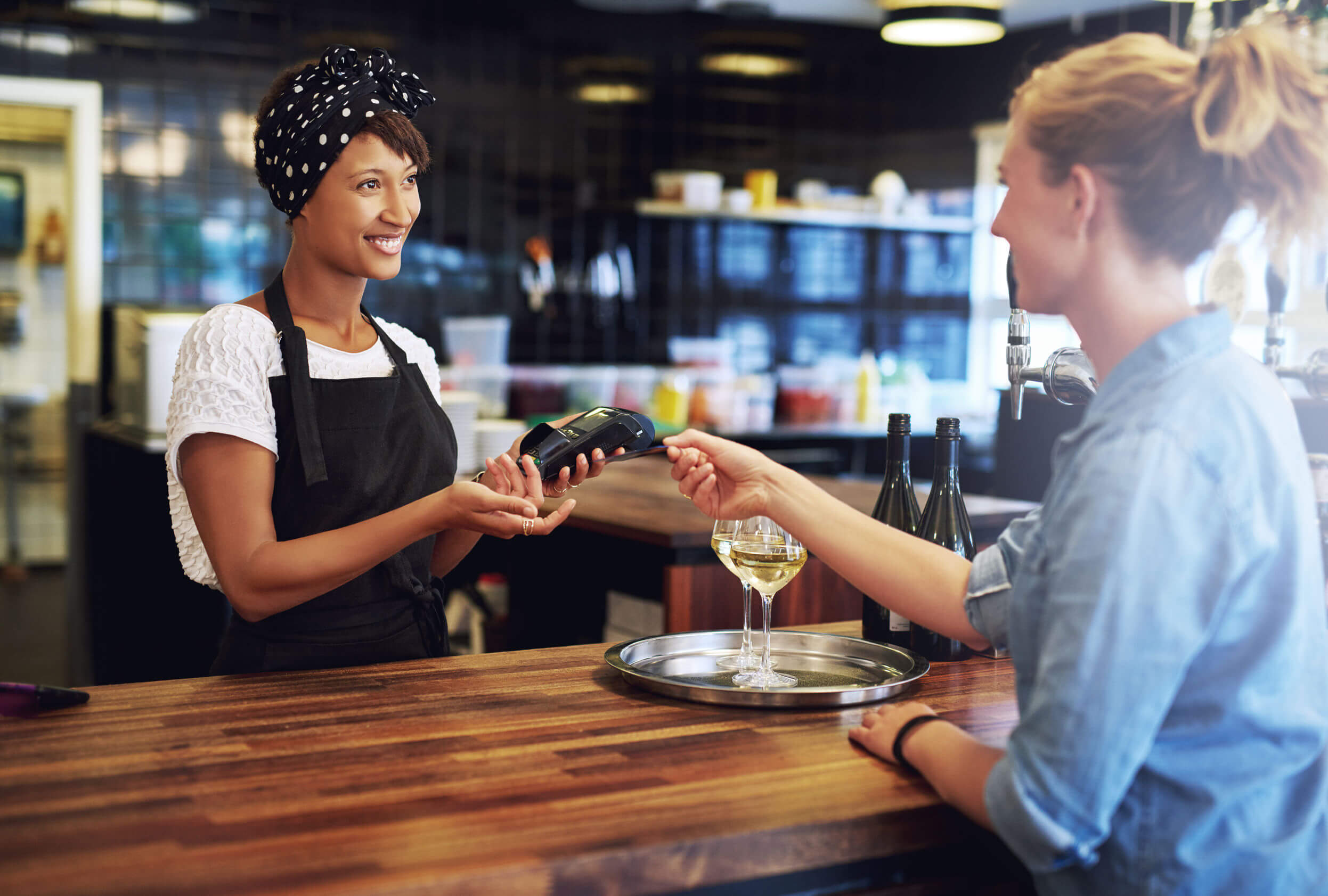 Customer in a pub paying the business owner or waitress with a credit card to be processed on a handheld banking machine, focus to the attractive african american owner