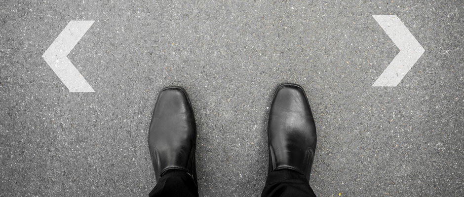 view looking down on a pair of business shoes standing between two arrows pointing in opposite directions