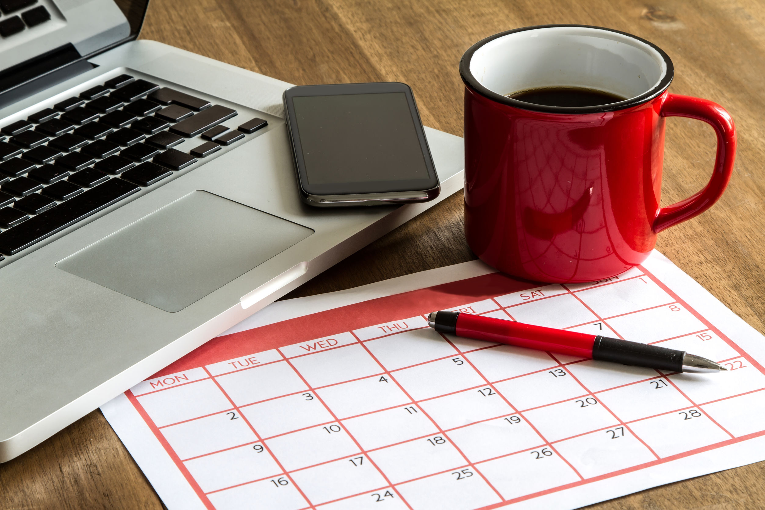 A picture of a calendar next to a laptop, smartphone and cup of coffee