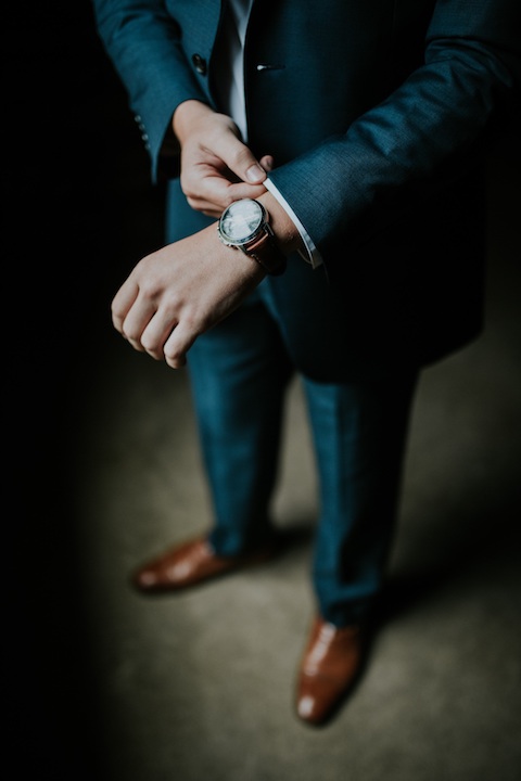 Man wearing a dark suit and brown shows checking the time on his wrist watch