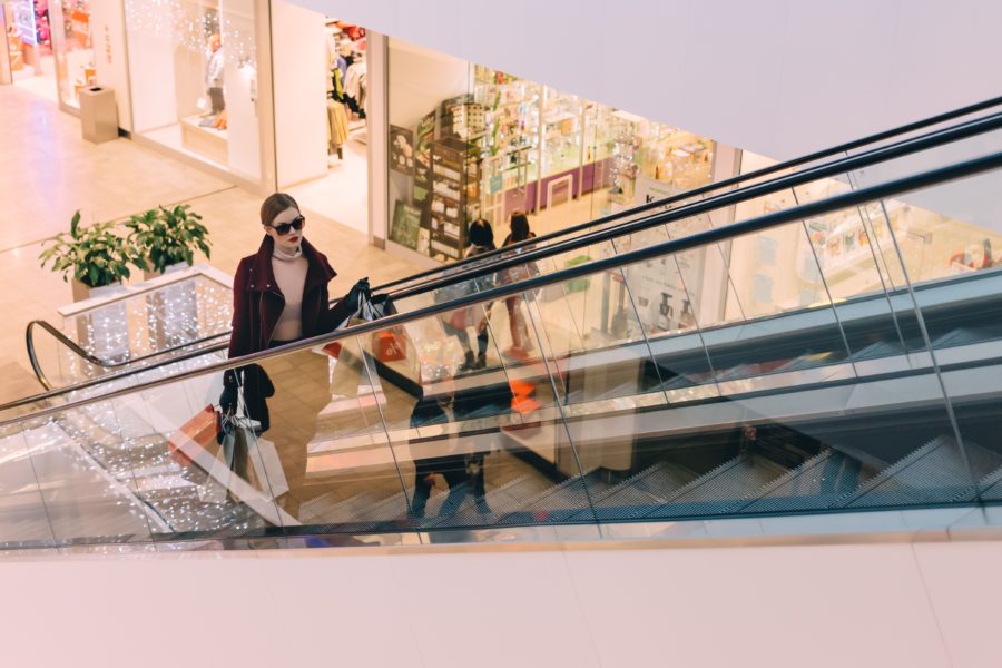 woman shopping at a mall going up an escalator with shopping bags