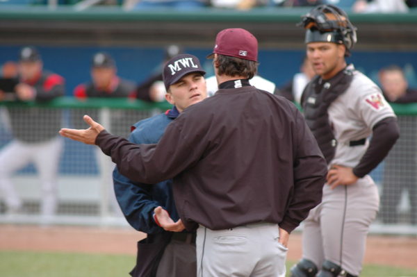 A baseball manager argues with the umpire during a baseball game as the catcher looks on