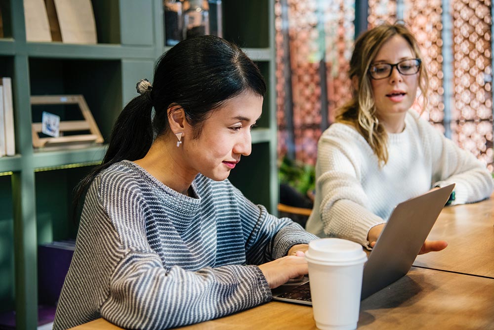 user rights woman using laptop on table with other woman pointing at laptop