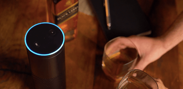 Johnnie Walker whiskey bottle, hand holding glass of whiskey and Amazon Alexa device