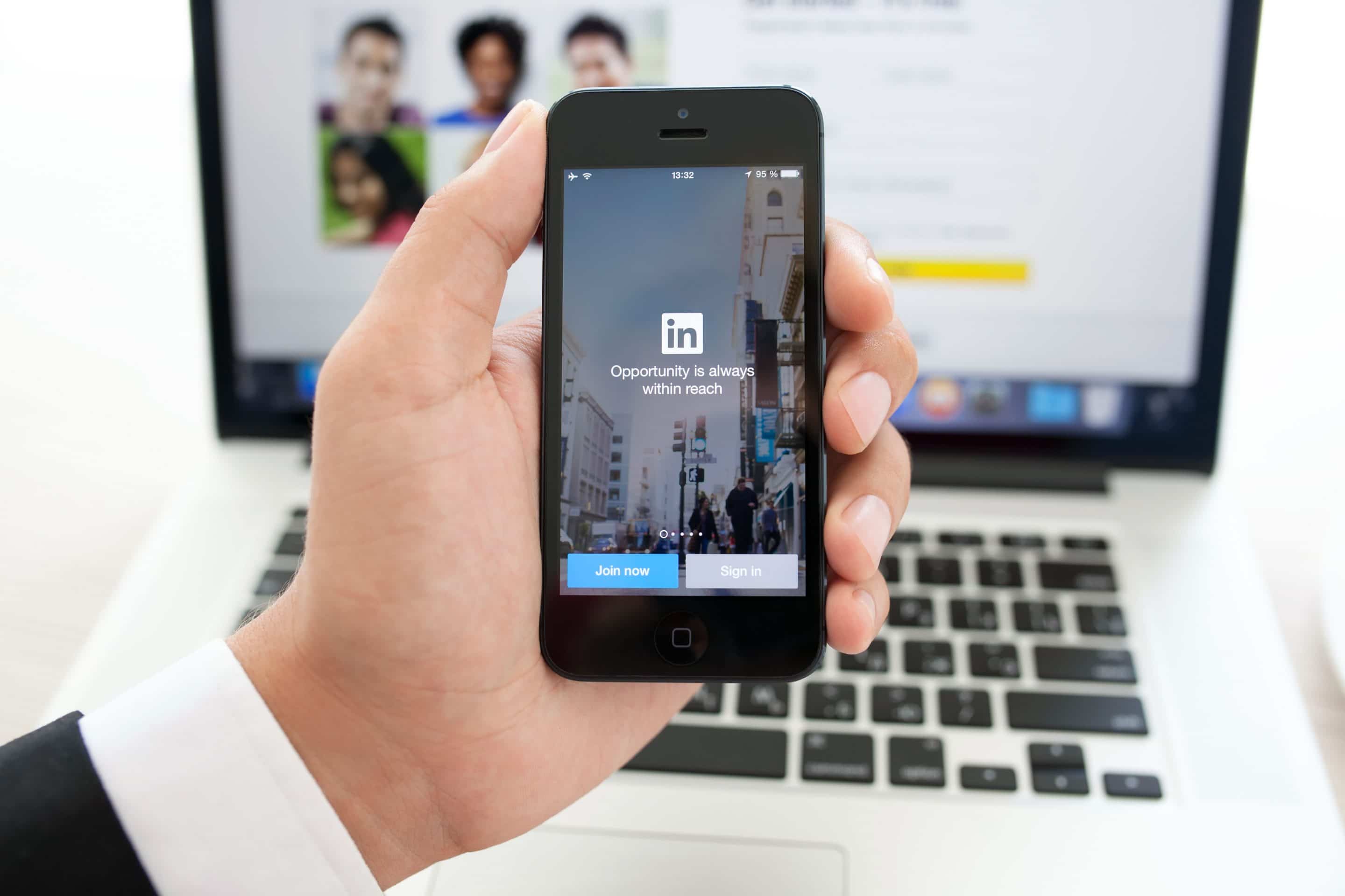 A business person holding a cell phone with a LinkedIn app.