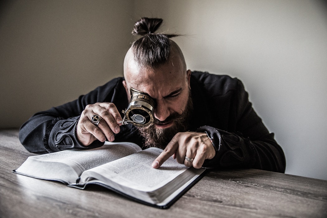 man using a magnifying glass to search through a book