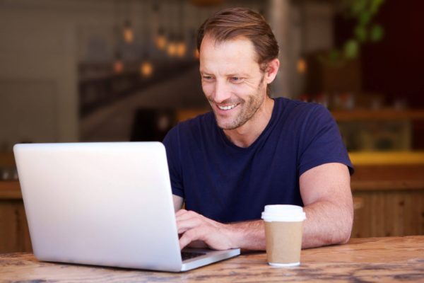 Man smiling at his laptop as he receives a relational email.