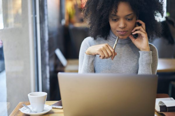 Young woman gazing at laptop and holding pen.
