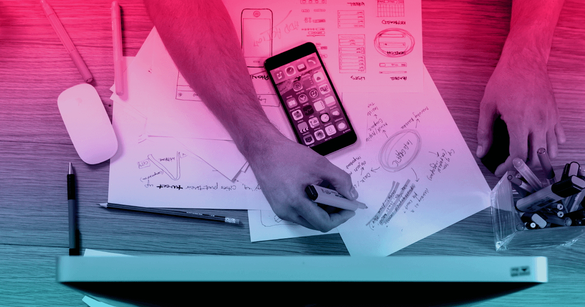 An overhead view of a persons desk. Their hands are visible, holding a highlighter. Next to a number of documents is a cell phone. The person may be working on an answer to the question, "What is digital marketing?"