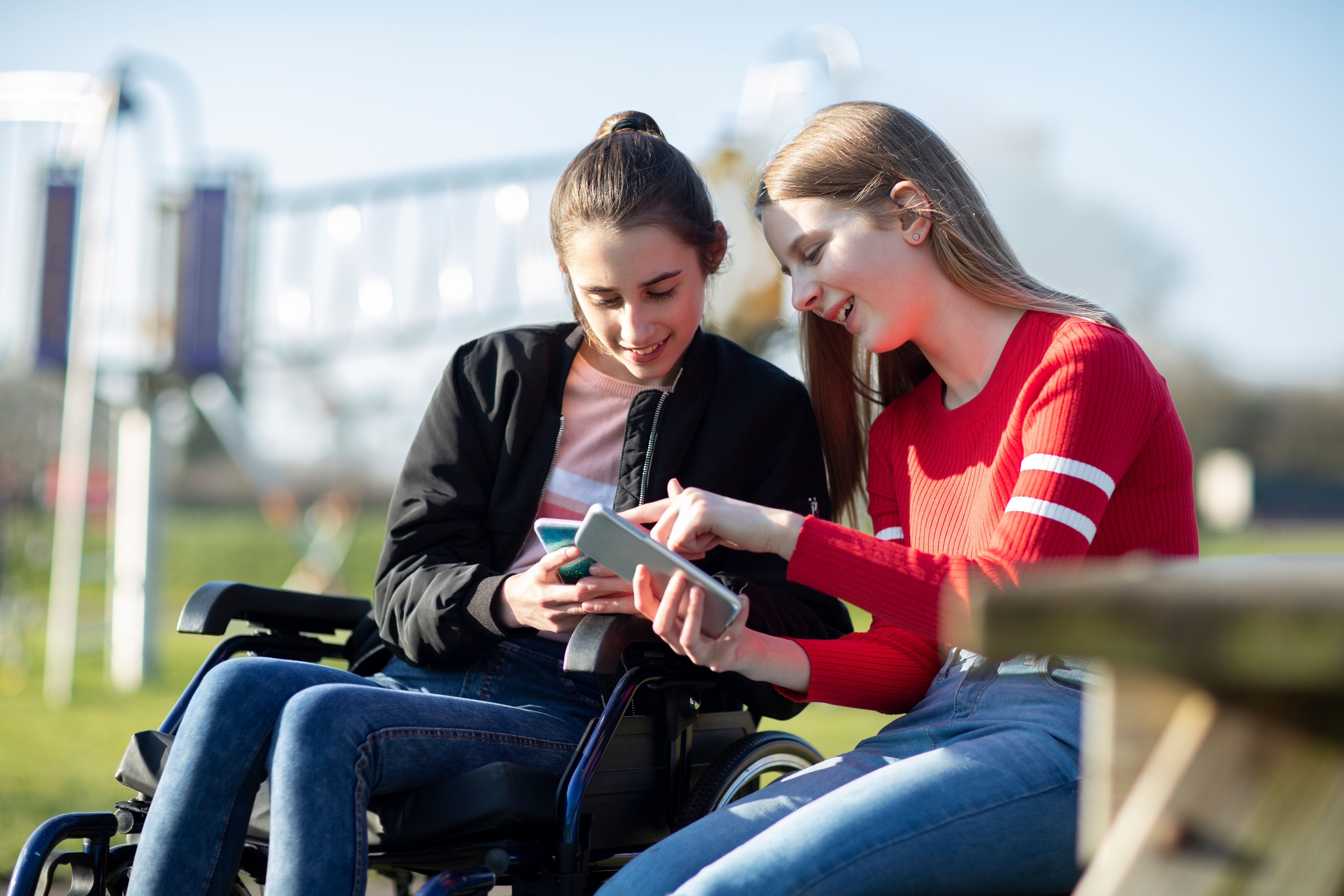 Two teenage girls looking down at phones and smiling.