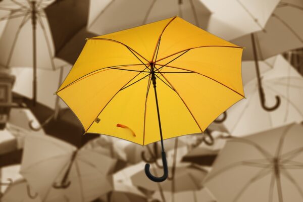 An image of umbrellas, the centre umbrella is bright yellow and the other umbrellas are grey