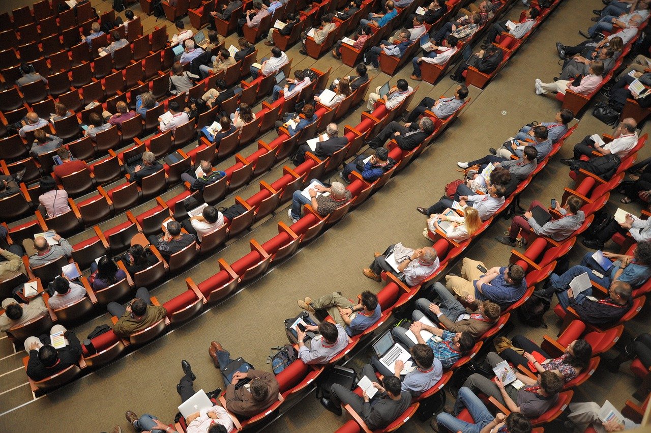An audience seated in curved rows at a meeting hall.