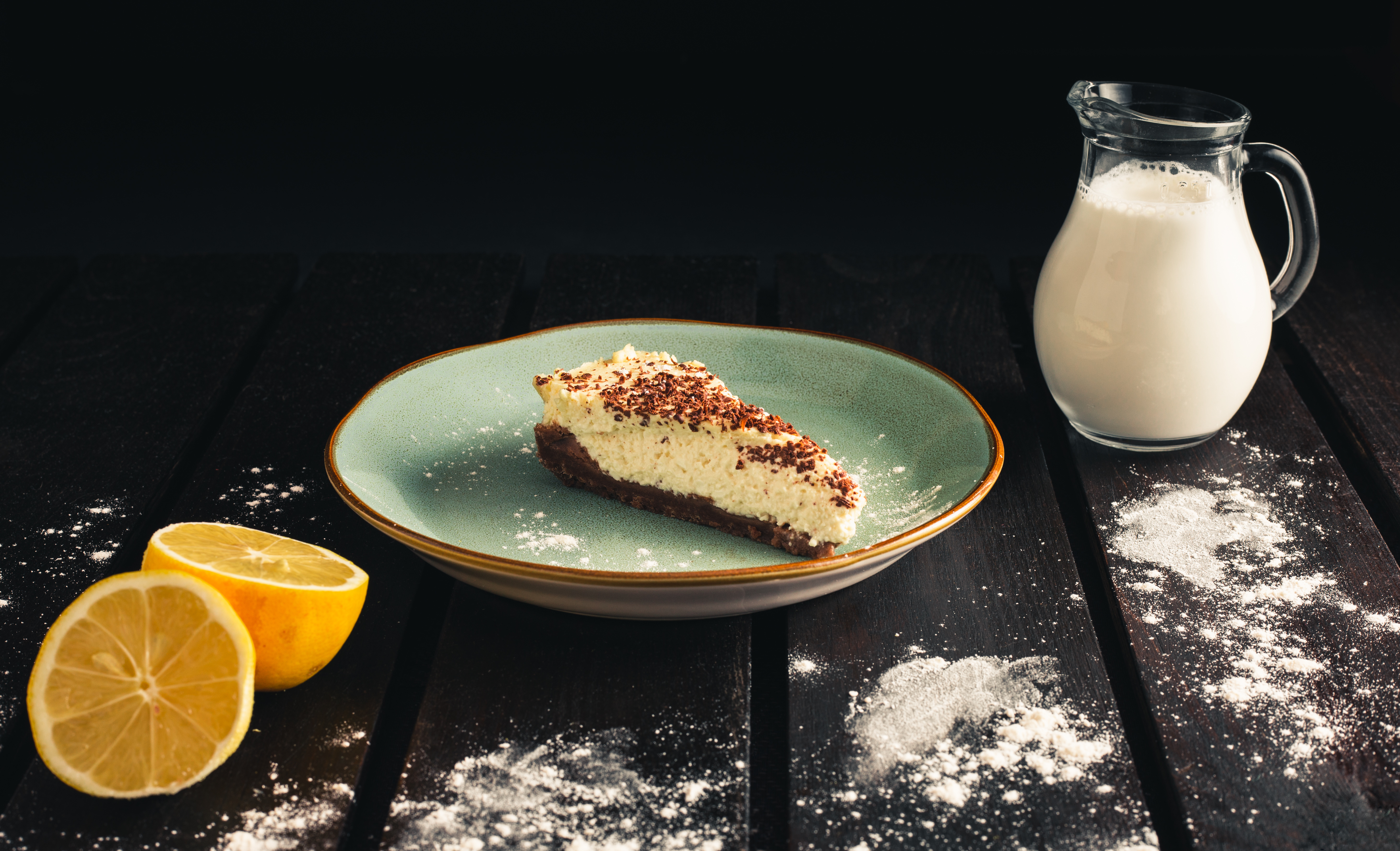 Product photo of chocolate bio cheesecake with lemon, milk, caster sugar on wooden background. Dark food Photography of sweet and illuminated dessert.