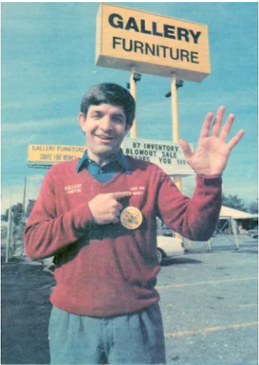 young mattress mack in front on gallery furniture sign