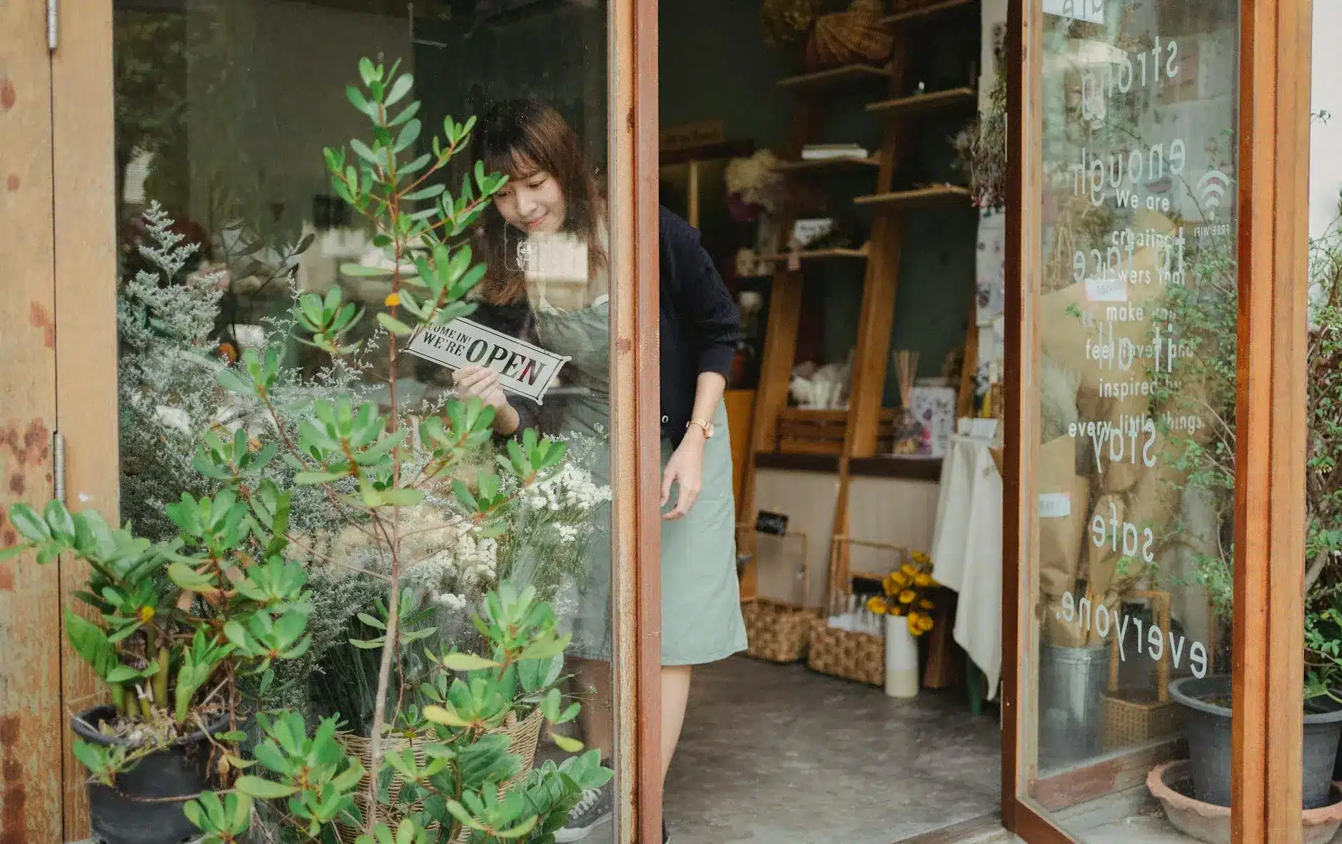 A woman opening a retail store door with a sign that reads 'Come in, we're open.'