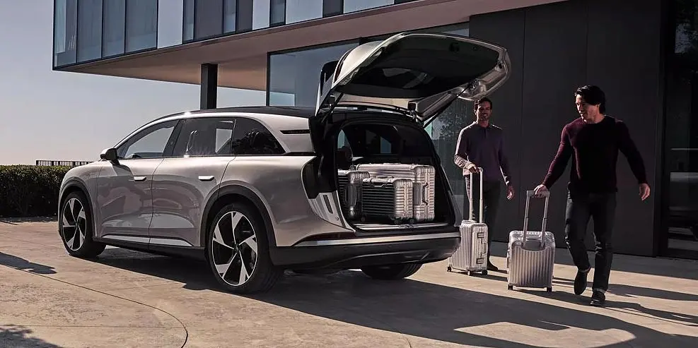 Two men pulling luggage from the trunk of a stylish silver SUV outside a modern building.