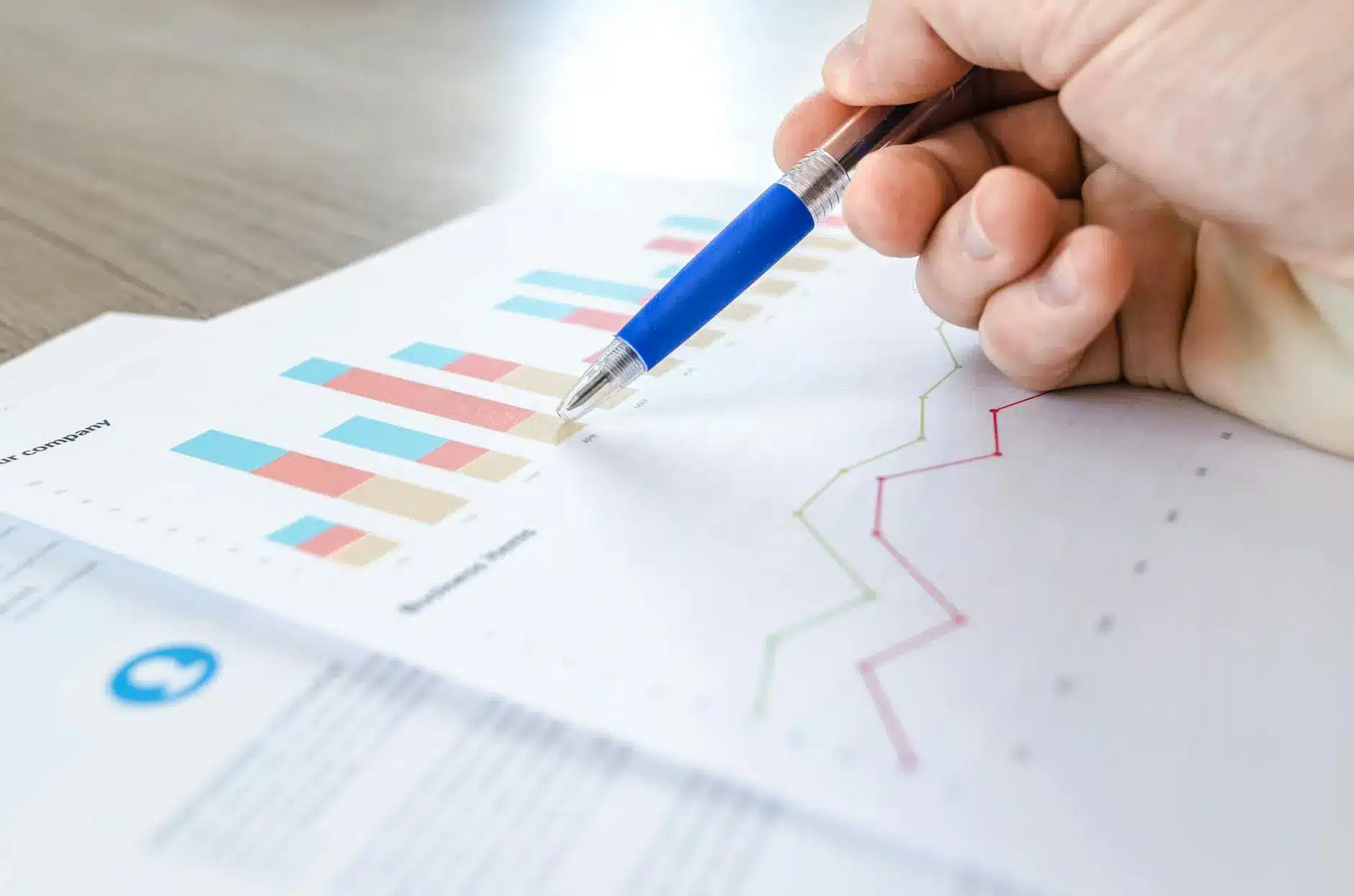 A hand pointing at colorful financial charts on paper.