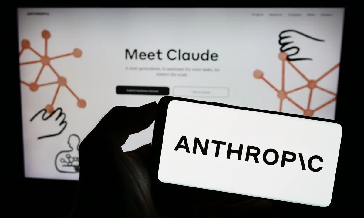 Hand holding a phone displaying the word 'ANTHROPIC' with a background featuring the Claude AI interface.