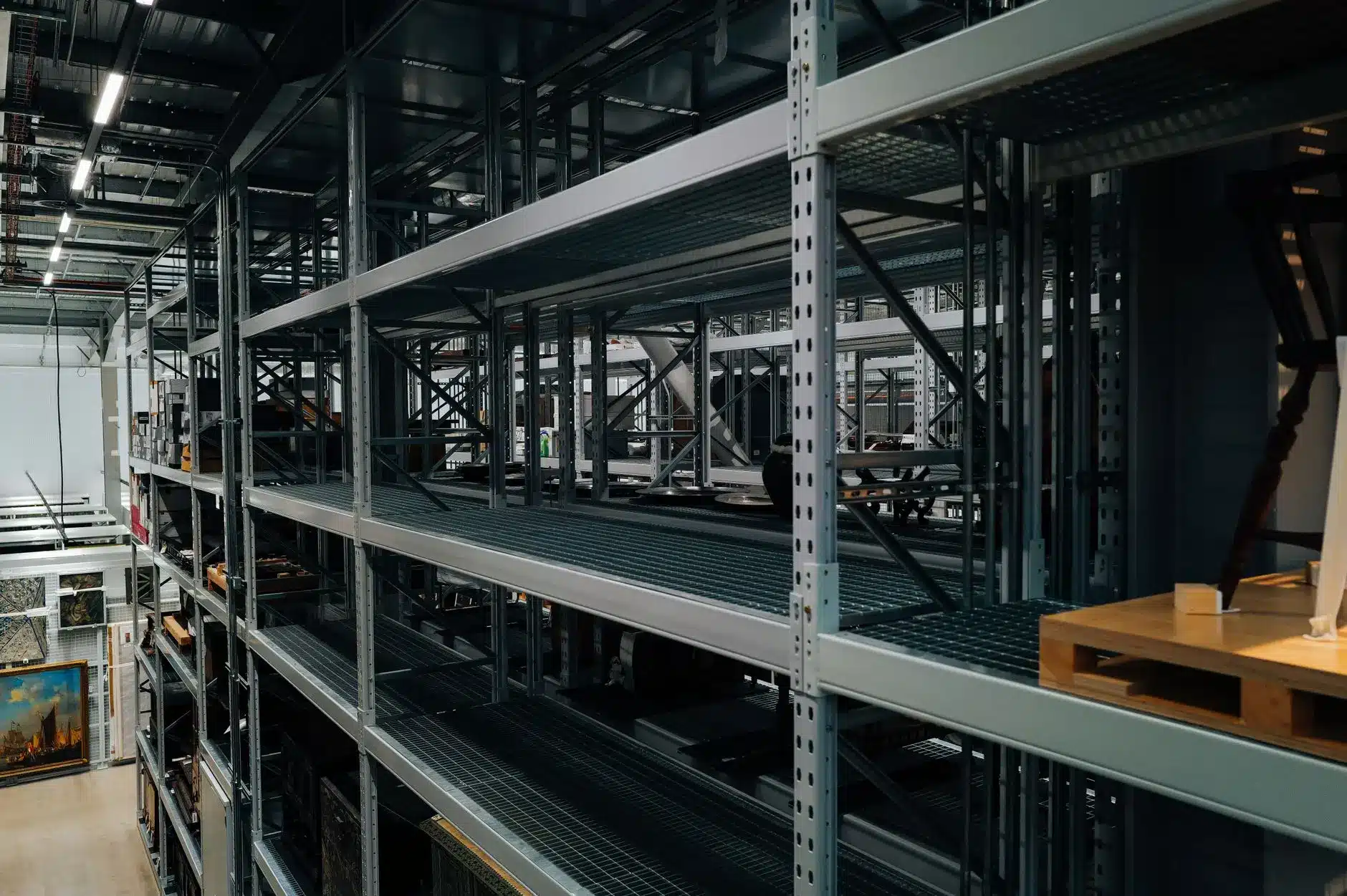 Empty warehouse storage shelves with few items and artwork in the background.