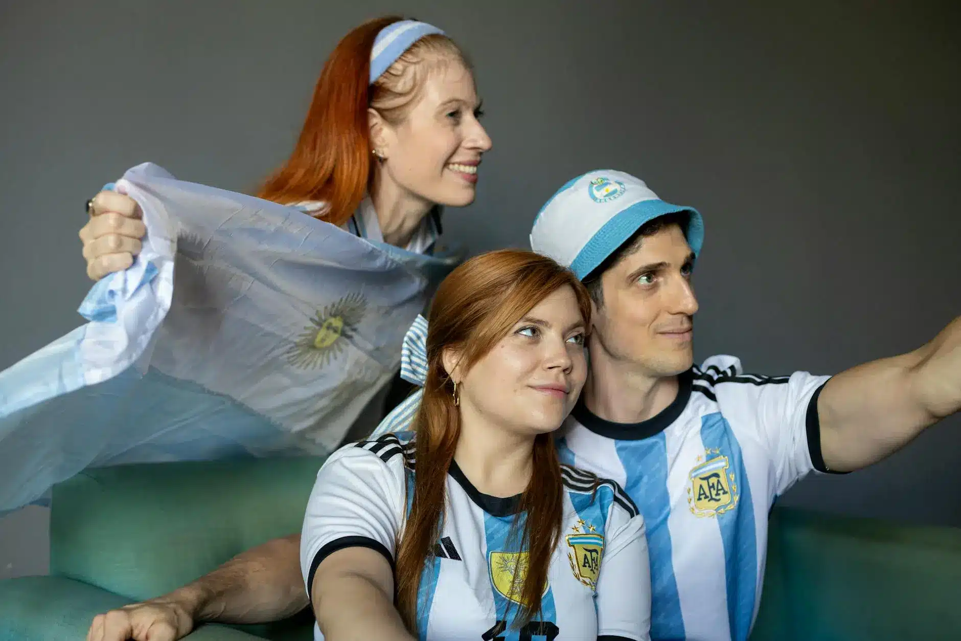Three fans wearing Argentina soccer jerseys cheer with a flag.
